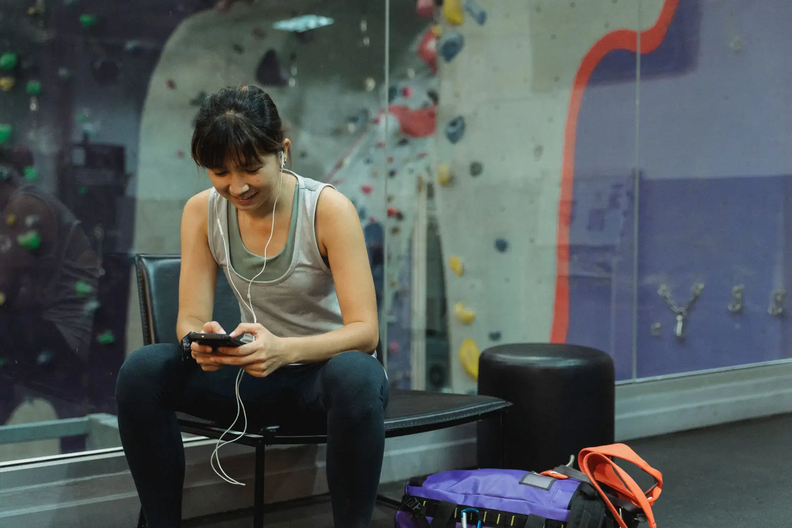 A woman checking her phone during a break at an indoor climbing gym