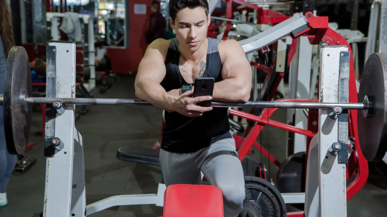 A man checking his phone beside a barbell in a gym